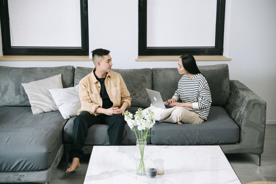 Man and woman discussing while working on a laptop in a stylish living room, creating a warm, casual atmosphere.